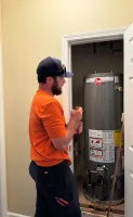 Estes Plumber performing maintenance of  water heater inside a utility closet with an open white door.