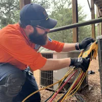 Estes Services Technician in orange uniform and cap repairing an AC in Alpharetta, Georgia