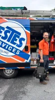 Bearded technician in orange uniform standing by an Estes Services van loaded with tools and equipment outdoors.