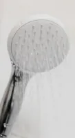 Fluctuating Temperature Close-up of a modern handheld showerhead spraying water in a white tiled bathroom.