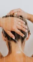 No Hot Water Person washing hair under running shower water with tattooed arm visible from behind.