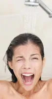 Delayed Hot Water Woman under shower water with eyes closed and mouth open, reacting to cold water splash in bathroom.