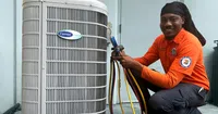Technician in Estes Services uniform smiling while servicing a Carrier air conditioning unit with tools and gauges.