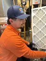 Estes Heating and Air Technician in orange shirt and blue cap installing a new air filter in a residential HVAC system.