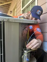Technician in orange uniform repairing an outdoor HVAC unit with tools and wiring focus.