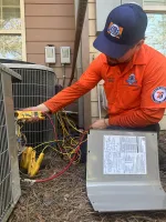 Estes Services HVAC technician in orange uniform using digital multimeter to service outdoor air conditioning unit with wiring and tools.