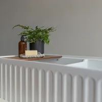 White bathtub with ridged exterior, wooden tray holding soap, amber bottle, and small green plant in black pot.