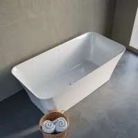 Modern white freestanding bathtub with rolled towels in basket on gray concrete floor and wall.