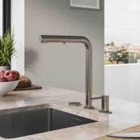 Modern stainless steel kitchen faucet with single handle on marble countertop next to window and fruit bowl.