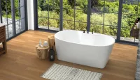 Modern bathroom with freestanding white bathtub, wooden floor, natural decor, and large glass windows overlooking greenery.