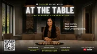 Woman sitting at table in documentary promo titled At The Table with real stories and lives impacted.