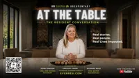 Smiling woman sits at a table with walnut decor, promoting EverResi documentary At The Table and its resident conversation.