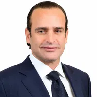 Professional man in a navy suit and tie with a white shirt against a white background.