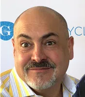 Smiling bald man with mustache and beard wearing a yellow striped shirt against a white background.