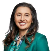 Smiling woman with long dark hair wearing a teal blazer and patterned shirt on white background