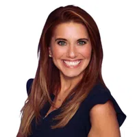 Smiling woman with long red hair wearing a navy blue sleeveless top against white background