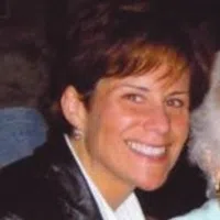 Smiling woman with short brown hair wearing a black jacket and white shirt in a dimly lit setting.