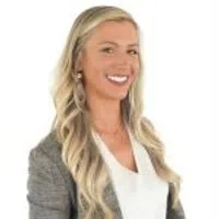 Professional woman with long blonde hair in business attire smiling against a white background.
