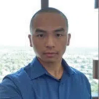 Man wearing blue shirt taking a selfie in front of a window with cityscape view in background
