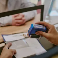 Hand stamping an approved mark on documents with a blue rubber stamp at a service counter.