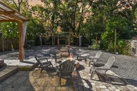 Outdoor backyard patio with fire pit surrounded by six chairs and string lights overhead at sunset.