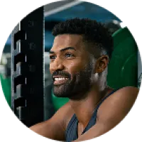Smiling man with beard and curly hair lifting weights in a gym with green weight plates in background