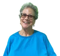Smiling elderly woman wearing glasses and a bright blue t-shirt against a white background.