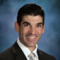 Professional man in dark suit and tie smiling against a blue textured background portrait