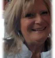 Smiling middle-aged woman with blonde hair wearing a white top in a close-up portrait.