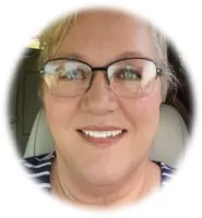 Close-up of smiling woman with glasses and light hair inside a car, wearing a striped shirt.