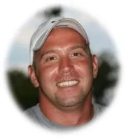 Smiling man wearing a white baseball cap and gray shirt with blurred outdoor background