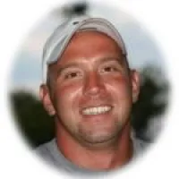 Smiling man wearing a white cap outdoors with blurred greenery and sky background in a circular frame.