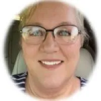 Smiling woman with glasses and blonde hair wearing a striped shirt sitting inside a car.