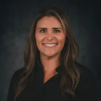Smiling woman with long brown hair wearing a black shirt against a dark gray background