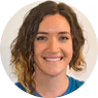 Smiling woman with curly brown hair wearing a blue shirt against a plain background