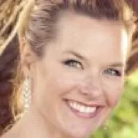 Close-up of a smiling woman with blonde hair and earrings outdoors in natural light.
