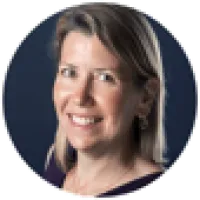 Portrait of a smiling middle-aged woman with shoulder-length blonde hair and a dark background.