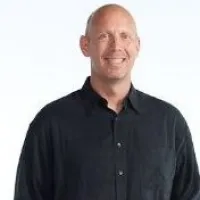 Smiling man in a black shirt against a light background, conveying a friendly vibe.