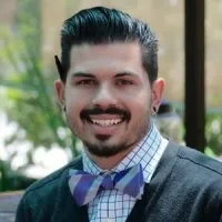 Young man with a stylish bow tie, smiling confidently in a green garden setting.