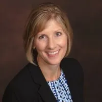 A professional portrait of a woman with short blonde hair, smiling in a business suit.