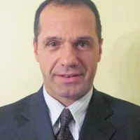 Professional man in a suit with a neutral expression and styled hair against a light background.