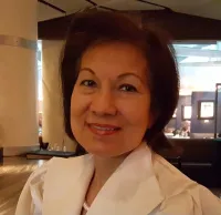 A smiling woman with dark hair wearing a white blouse in a restaurant setting.