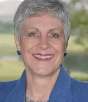 Woman with short gray hair smiling against a scenic outdoor background.