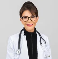 Smiling female doctor in glasses and white coat with a stethoscope, against a neutral background.
