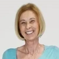 Smiling mature woman with short blonde hair wearing a light blue top against a plain background