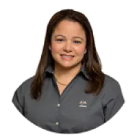 Smiling woman with long brown hair wearing gray collared shirt with embroidered logo on white background