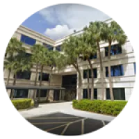Modern office building with large windows, palm trees, and clear blue sky in a sunny setting