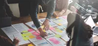 Team collaborating over printed documents and colorful sticky notes during a brainstorming session at a wooden table.