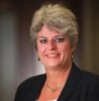 Smiling woman with short gray hair wearing a dark blazer in a professional indoor setting