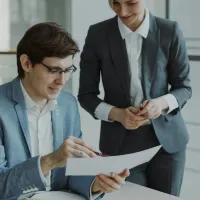 Two professionals in business attire reviewing a document together in a modern office setting.